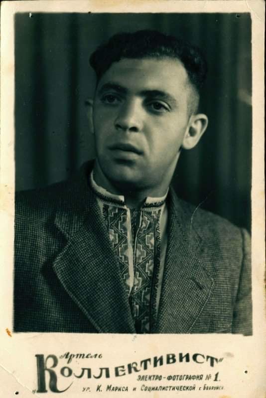 Lev Bolotnikov, 1959. Black and white photo of stern-faced young man with dark hair, a tunic with geometric patterns visible under his jacket